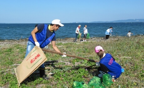 海岸で袋を手にごみ拾いをする従業員の様子の写真
