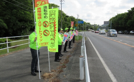 道路沿いで交通安全の黄旗を掲げ立哨する様子の写真