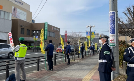 街中の歩道で黄旗を掲げ交通安全立哨を行う様子の写真